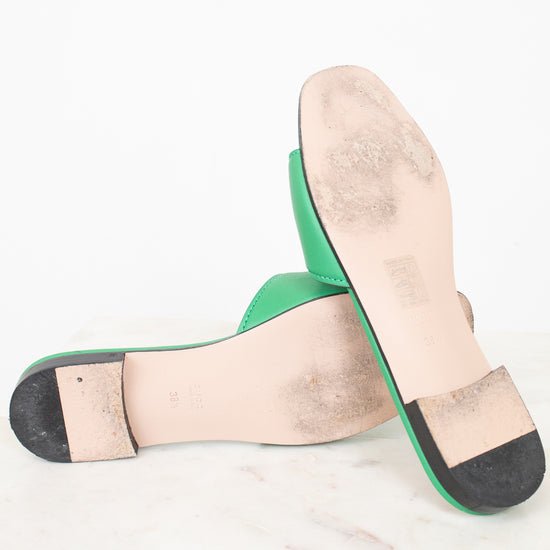 View of minimal wear to bottom soles of green slides displayed against a marble surface