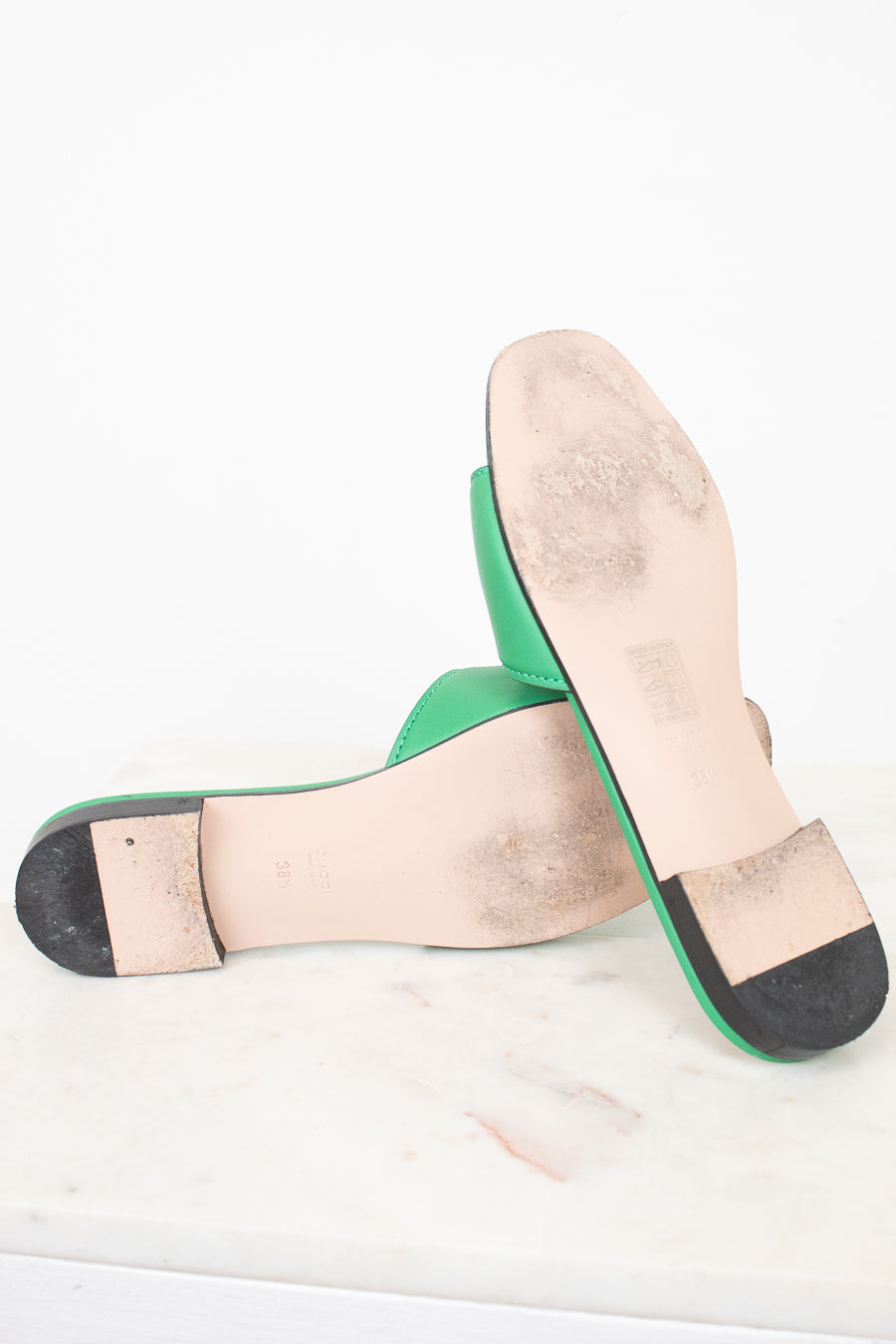 View of minimal wear to bottom soles of green slides displayed against a marble surface