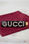 Black Gucci hair clip with rhinestones on a red fabric background