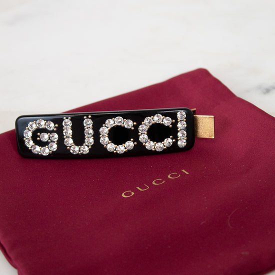 Black Gucci hair clip with rhinestones on a red Gucci pouch.