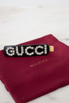 Black Gucci hair clip with rhinestones on a red Gucci pouch.