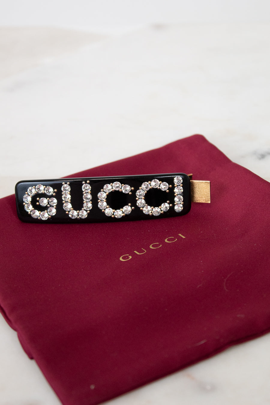Black Gucci hair clip with rhinestones on a red Gucci pouch.