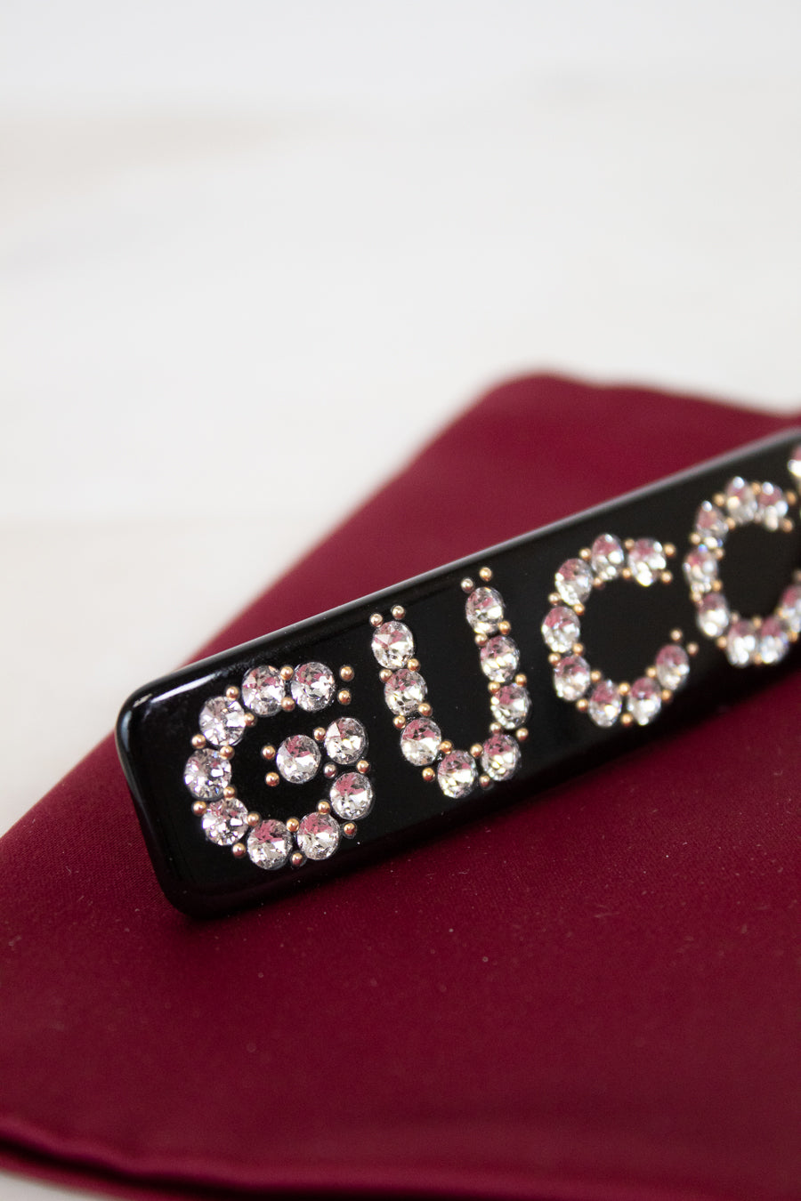 Black rectangular hair clip with 'GUCCI' in rhinestones on a red surface