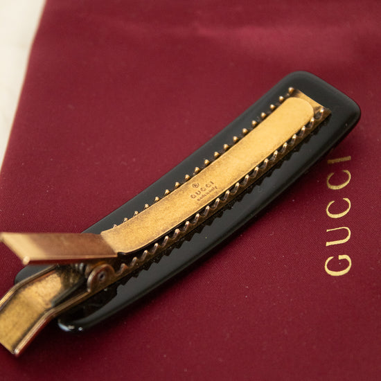 Gold clip with black resin on a Gucci branded red surface