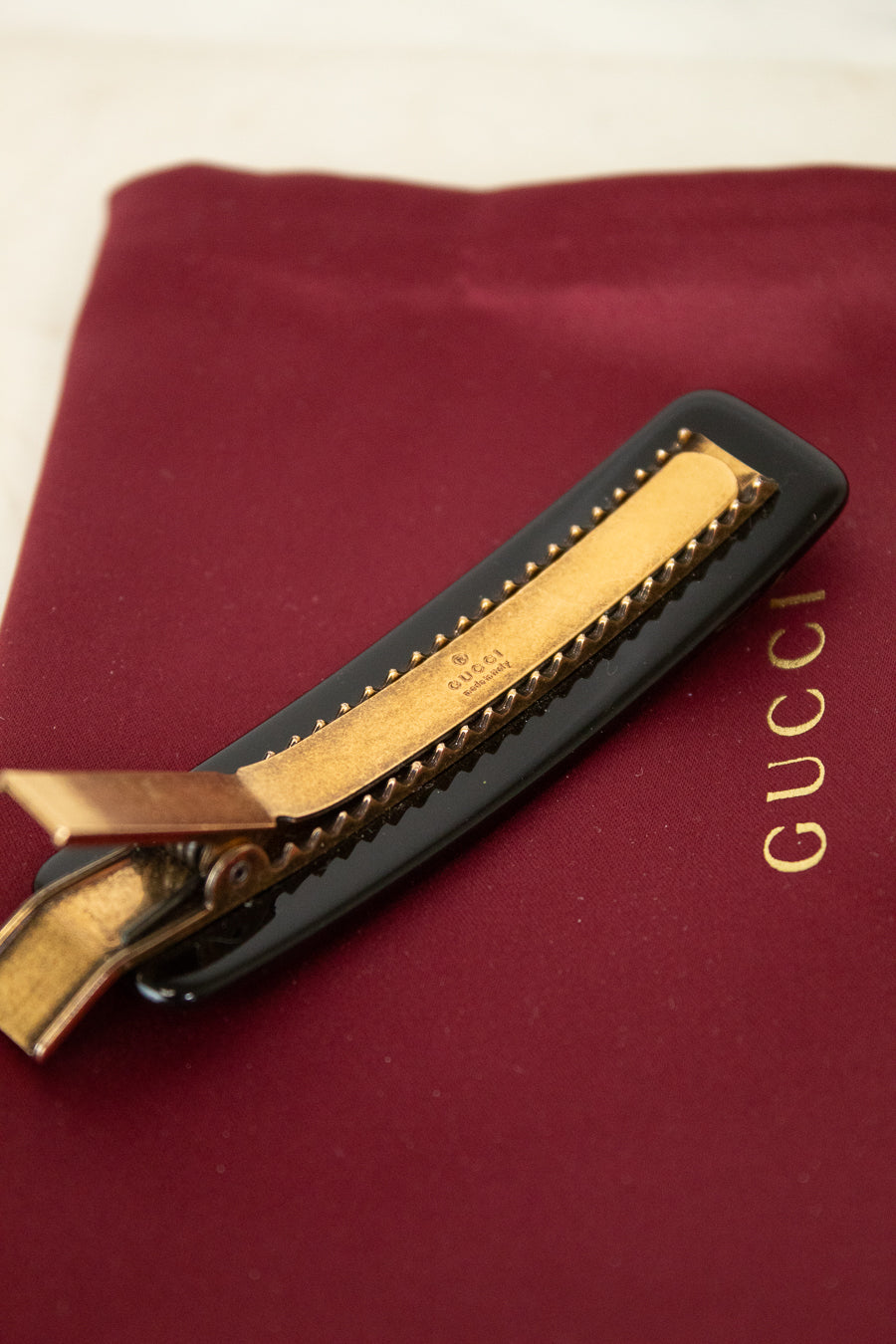 Gold clip with black resin on a Gucci branded red surface