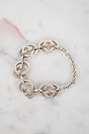 A silver-tone Gucci bracelet featuring interlocking GG logo links and a chain link closure, displayed on a white marble surface.