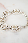 A silver-tone interlocking GG Gucci chain bracelet with oval chain links, displayed on a light marble surface. The brand is identified as Gucci due to the distinctive interlocking G logo pattern.