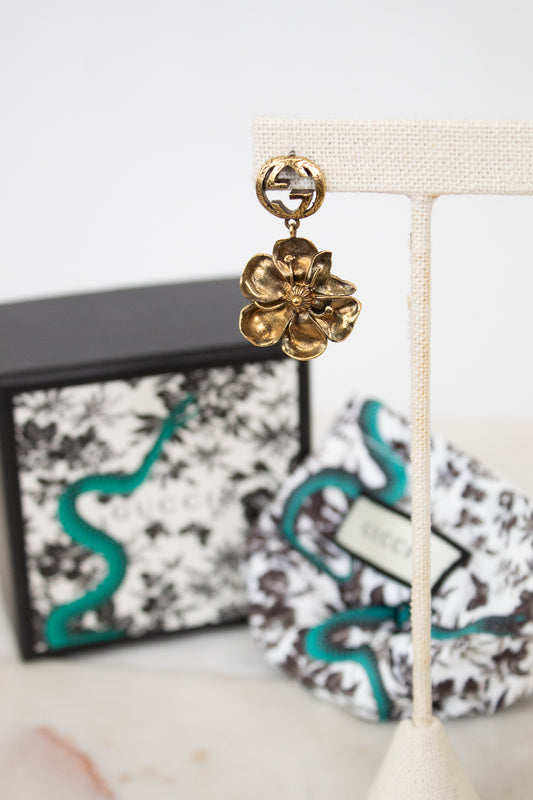 Gold floral earring on a white stand with a decorative box in the background