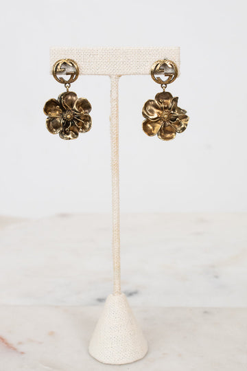 Gold floral Gucci earrings on a white stand with a marble background