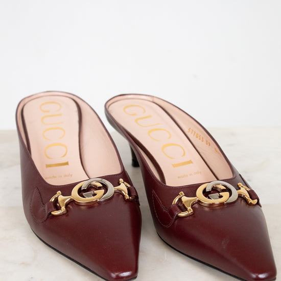 Pair of Gucci kitten heel shoes with gold and silver accents on a marble surface.