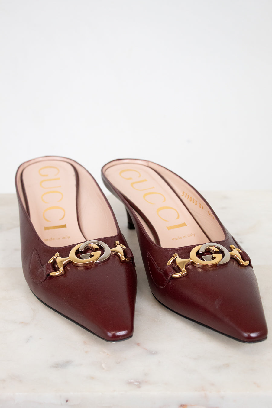 Pair of Gucci kitten heel shoes with gold and silver accents on a marble surface.