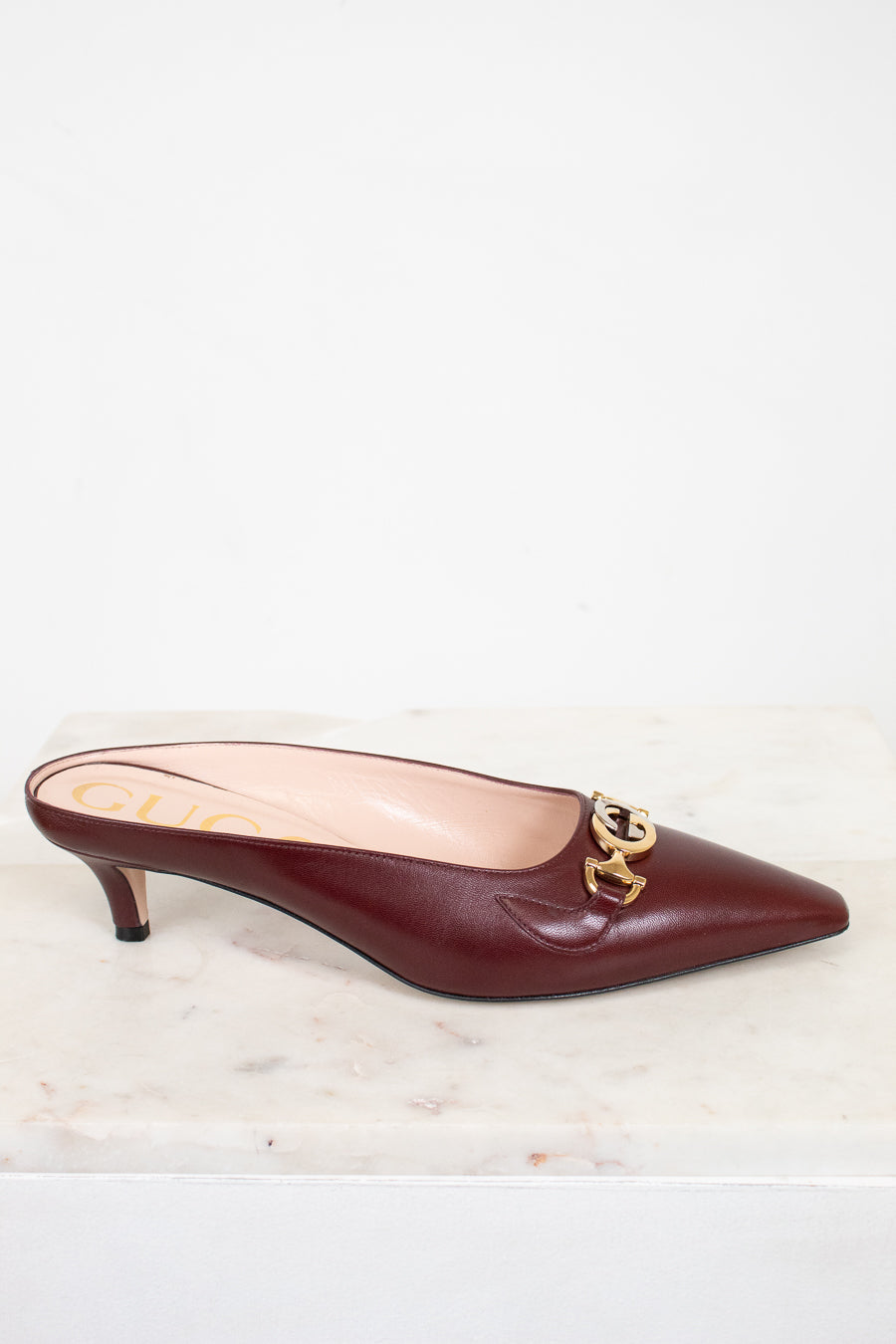 Maroon kitten heel shoe with gold and silver emblem on a light background