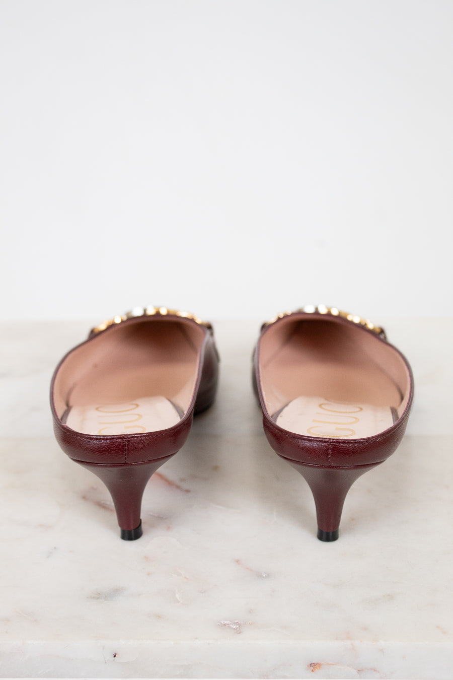 Pair of maroon kitten heel shoes on a light marble surface
