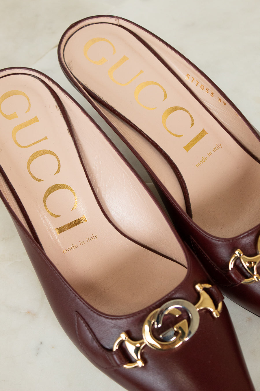 Maroon Gucci shoes with gold and silver logo on a light background