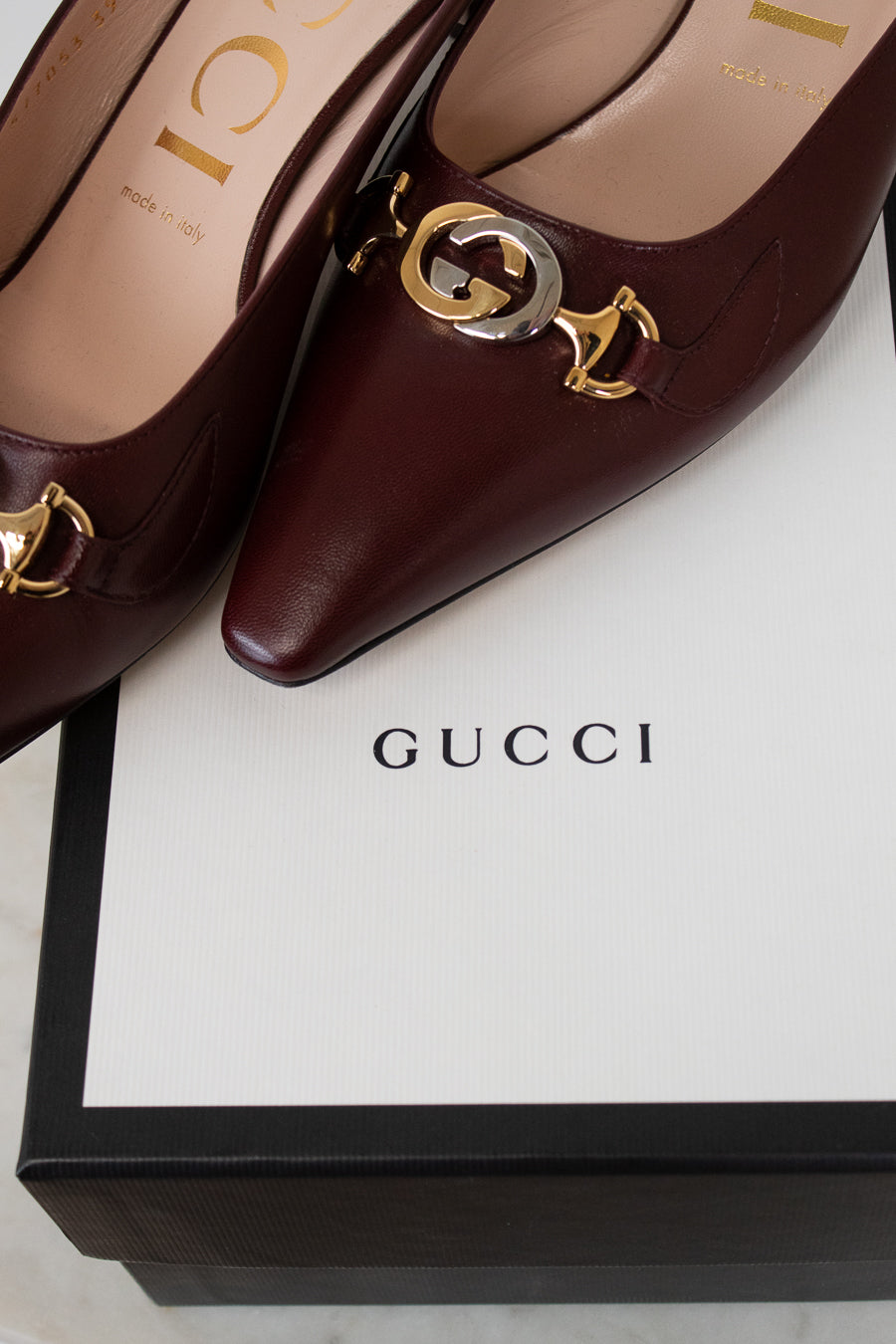 Maroon Gucci shoes with gold and silver accents on a Gucci box.