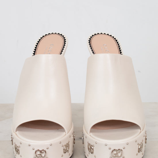 Pair of white sandals with decorative studs on a light background