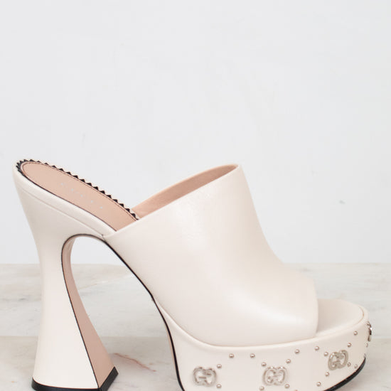 White high-heeled shoe with platform and decorative elements on a light background