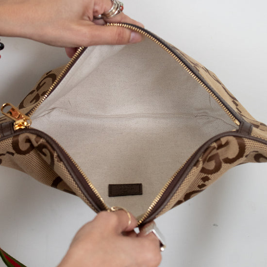 Close-up of a beige handbag with brown accents being opened from top view of a person against a white background