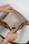 Close-up of a beige handbag with brown accents being opened from top view of a person against a white background