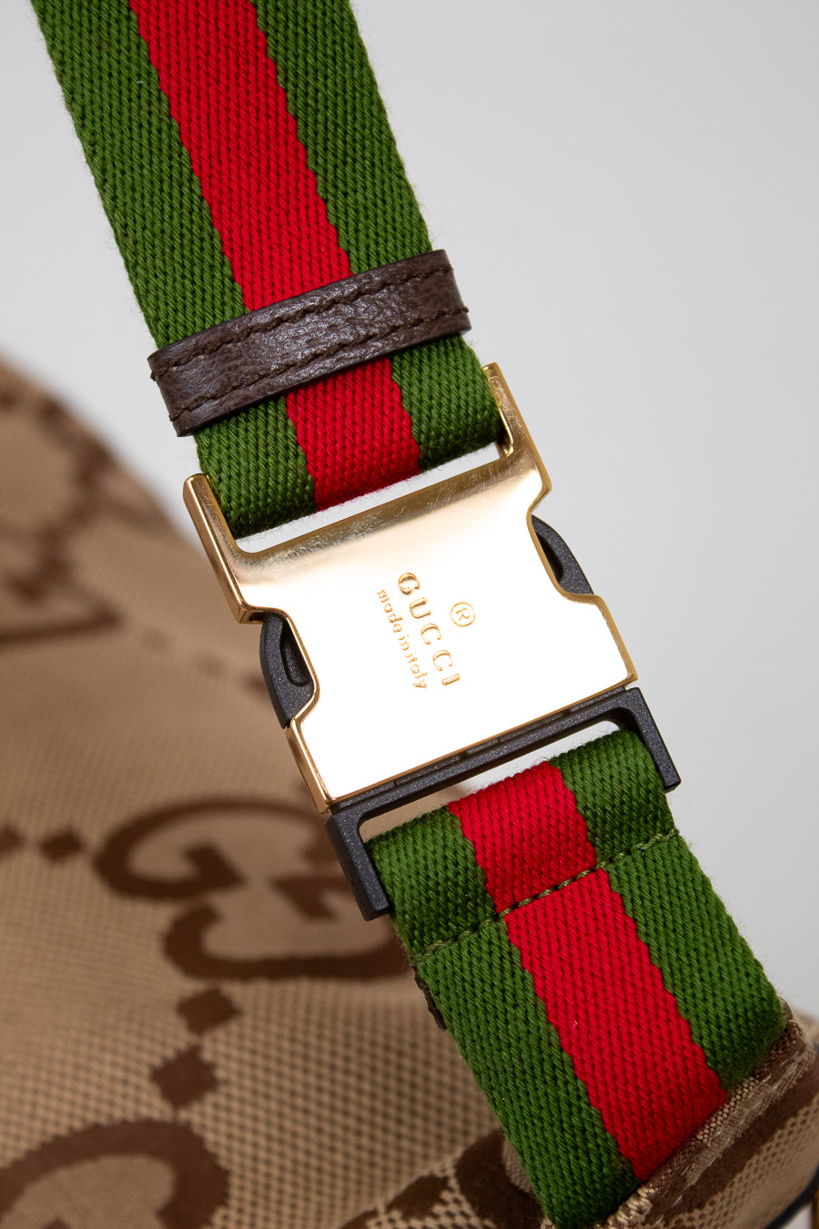Close up of gold tone Gucci stamped buckle closure with the red and green striped straps and monogram beige bag