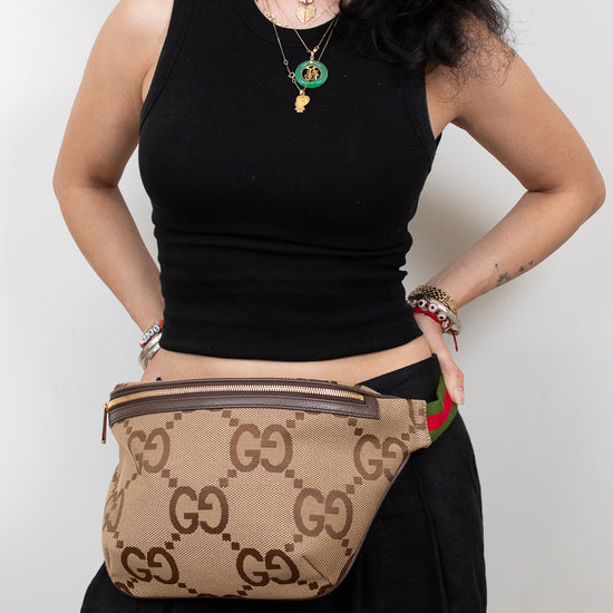 Person wearing a black sleeveless top and black pants with a beige Gucci belt bag.