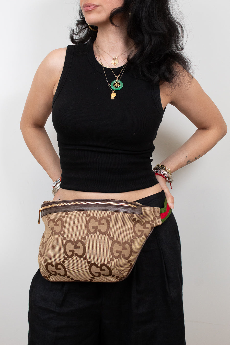 Person wearing a black sleeveless top and black pants with a beige Gucci belt bag.