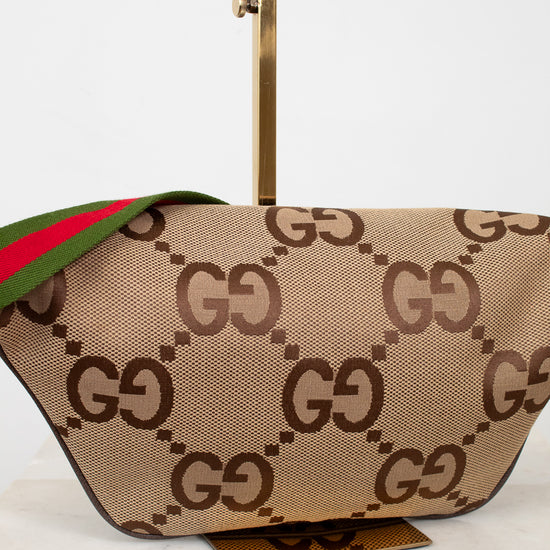 Back view of beige belt bag with large brown gucci monogram logo with a green and red striped strap on a white background