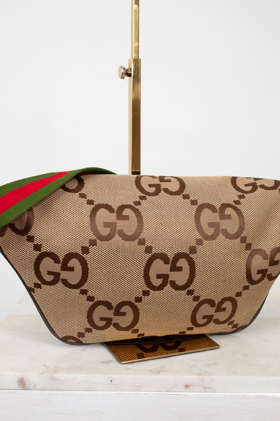 Back view of beige belt bag with large brown gucci monogram logo with a green and red striped strap on a white background