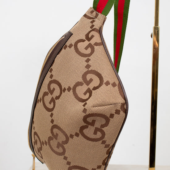 Front bottom view of beige belt bag with large brown gucci monogram logo with a green and red striped strap on a white background.