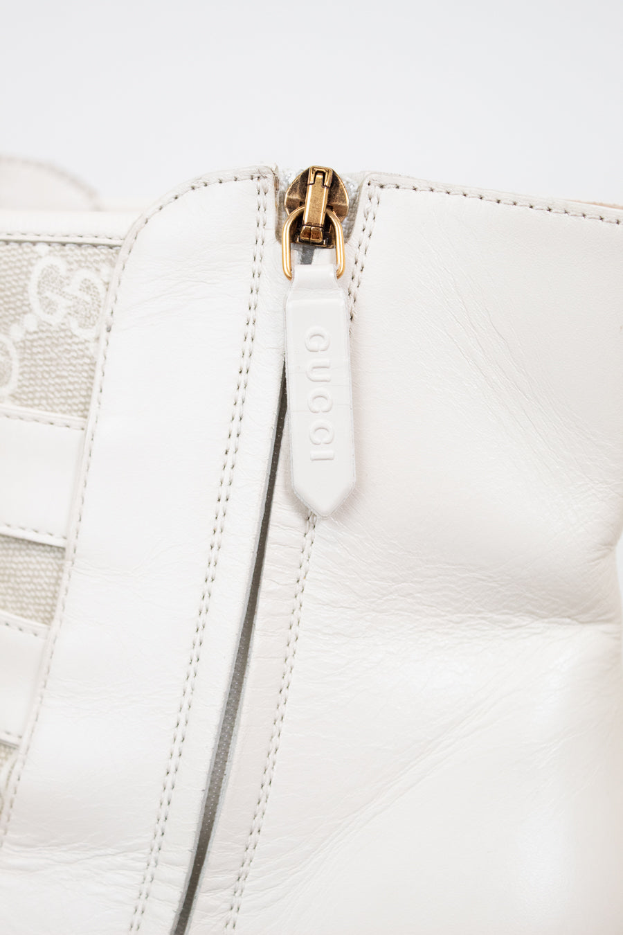 Close-up of a white leather jacket with a gold zipper on a light gray background