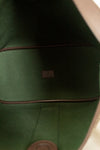 Close-up of the interior lining of a bag, showing dark green felt or fabric with brown trim and a small central brand patch.