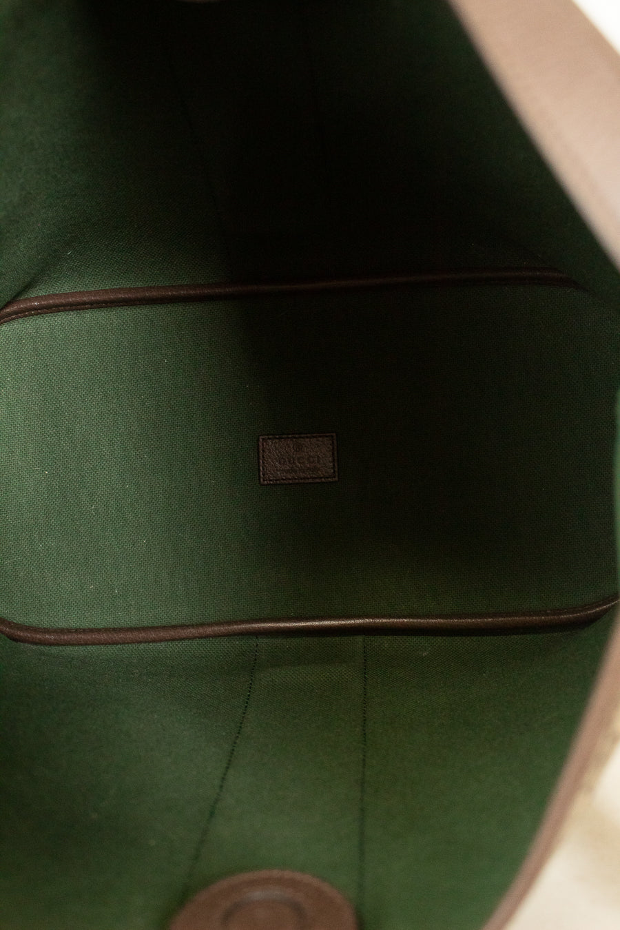 Close-up of the interior lining of a bag, showing dark green felt or fabric with brown trim and a small central brand patch.
