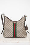 A Gucci monogram shoulder bag in beige GG canvas with the signature green and red web stripe down the center, dark brown leather trim and strap, and a gold-tone GG logo clasp, displayed on a white marble surface against a white background.