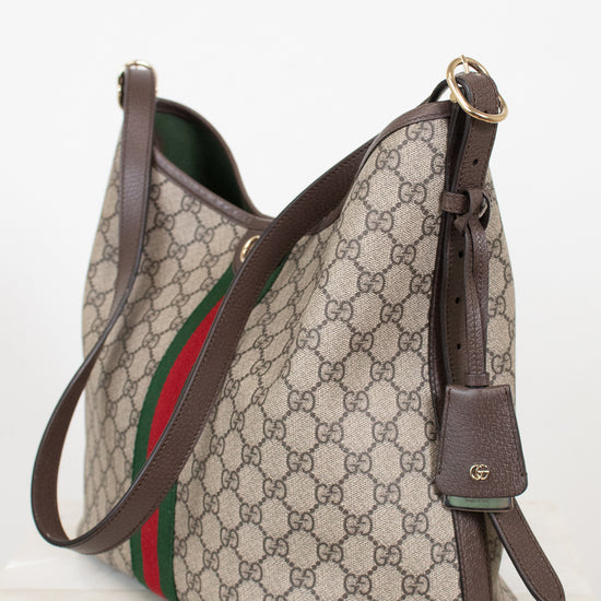 Gucci GG Supreme canvas shoulder bag with brown leather trim, a green and red web stripe, and gold-tone hardware, photographed on a light neutral background.