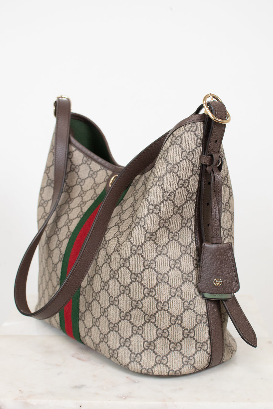Gucci GG Supreme canvas shoulder bag with brown leather trim, a green and red web stripe, and gold-tone hardware, photographed on a light neutral background.