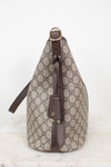 A Gucci shoulder bag in beige and brown GG Supreme canvas with dark brown leather trim and a gold-tone buckle, shown from the side on a light marble surface against a white background.