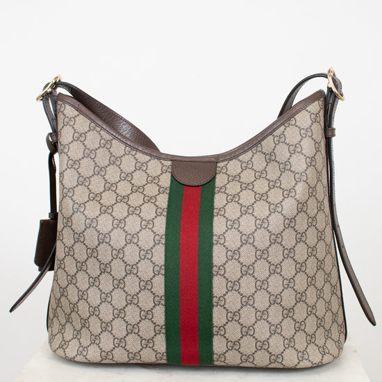 Gucci GG Supreme canvas hobo bag with brown leather trim and the signature green and red web stripe, displayed on a white marble surface against a white background.