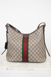 Gucci GG Supreme canvas hobo bag with brown leather trim and the signature green and red web stripe, displayed on a white marble surface against a white background.