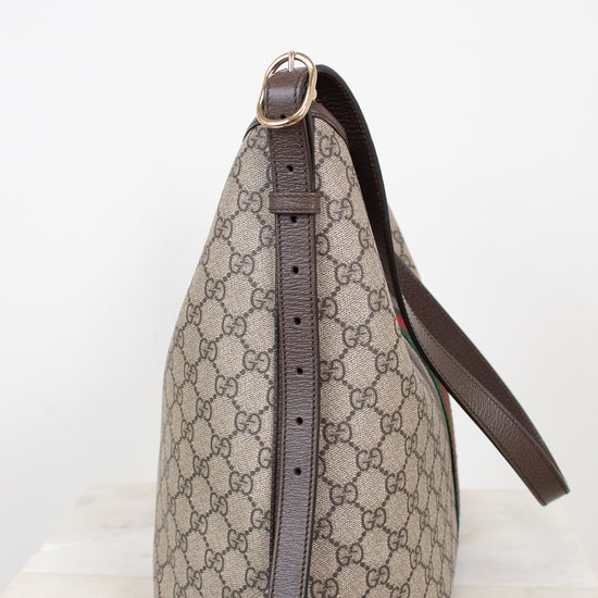 A Gucci shoulder bag in beige and brown GG Supreme canvas with dark brown leather trim and strap, shown on a light marble surface against a white background.