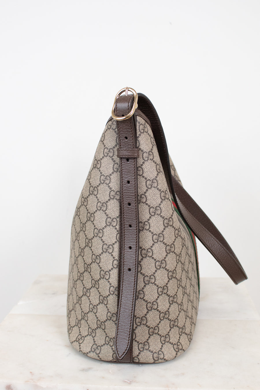 A Gucci shoulder bag in beige and brown GG Supreme canvas with dark brown leather trim and strap, shown on a light marble surface against a white background.