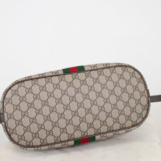 A Gucci monogram canvas pouch with a green and red web stripe detail, resting on a white marble surface against a white background.