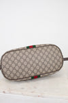 A Gucci monogram canvas pouch with a green and red web stripe detail, resting on a white marble surface against a white background.
