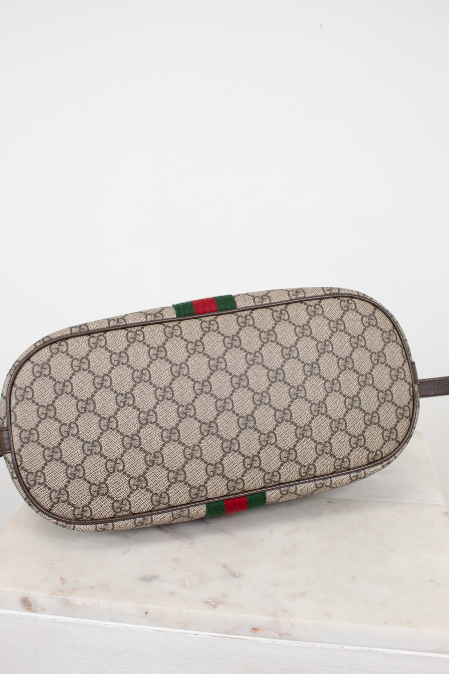 A Gucci monogram canvas pouch with a green and red web stripe detail, resting on a white marble surface against a white background.