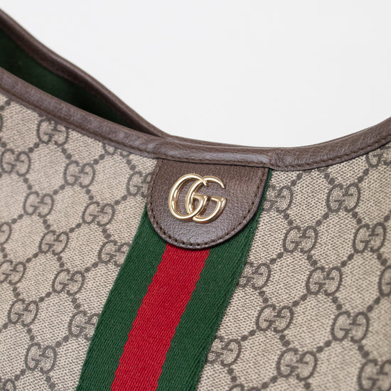 Close-up of a Gucci shoulder bag featuring the classic GG Supreme canvas, brown leather trim, a green and red web stripe, and a gold-tone interlocking GG logo on a leather tab.
