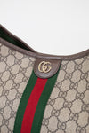 Close-up of a Gucci shoulder bag featuring the classic GG Supreme canvas, brown leather trim, a green and red web stripe, and a gold-tone interlocking GG logo on a leather tab.