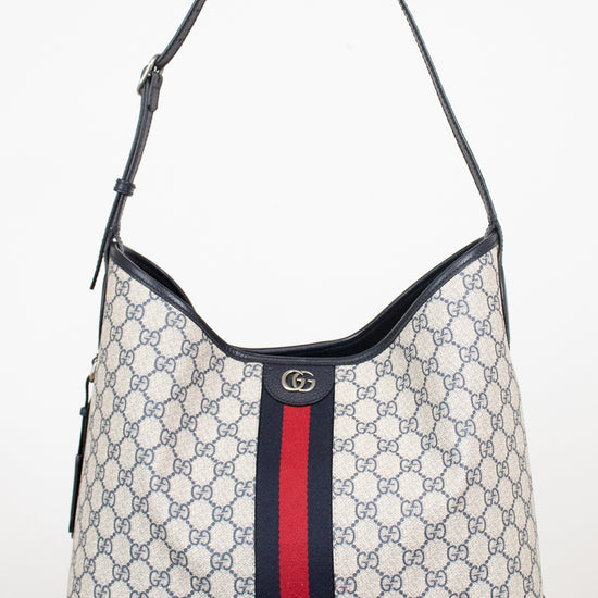 Monogrammed 'Gucci' tote bag showing red and navy center stripe with 'GG' hardware against a plain background