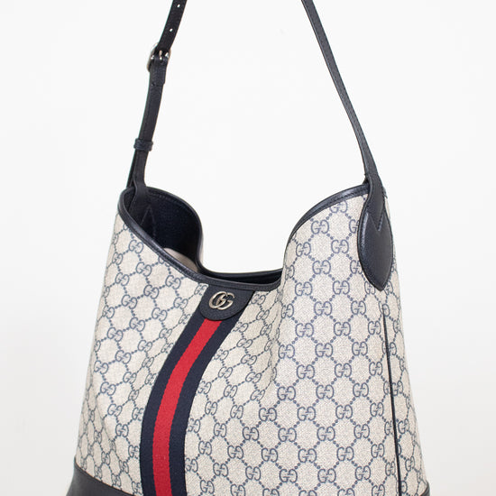 Monogrammed 'Gucci' tote bag showing red and navy center stripe with 'GG' hardware against a plain background