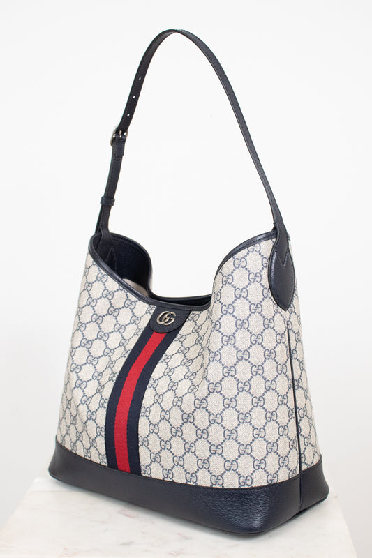 Monogrammed 'Gucci' tote bag showing red and navy center stripe with 'GG' hardware against a plain background