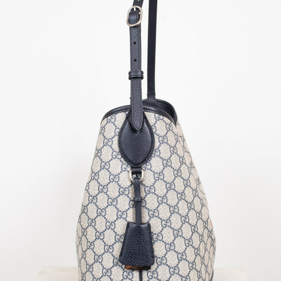 Monogrammed 'Gucci' tote bag showing  the side view with bag charm detailing against a plain background