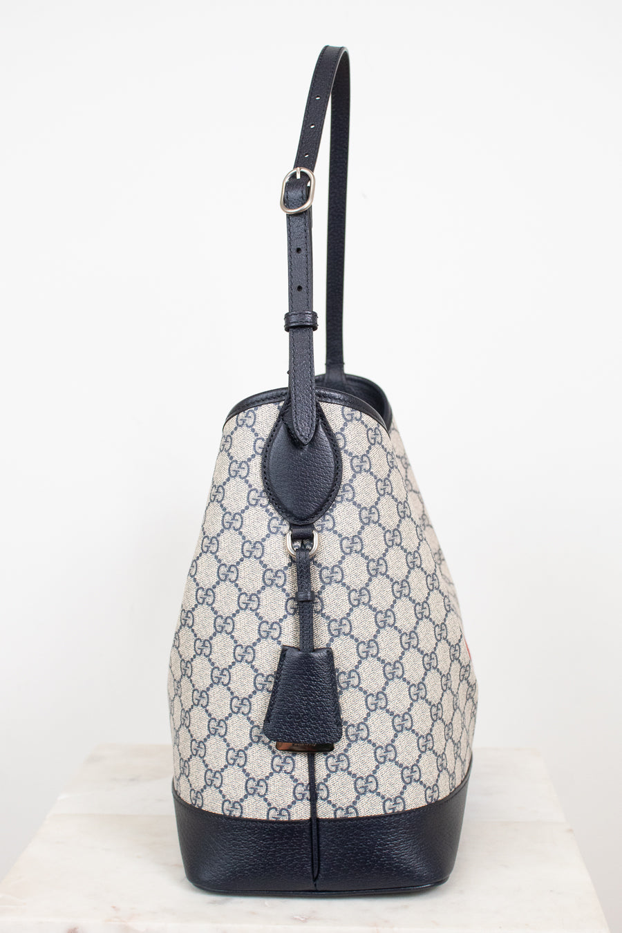 Monogrammed 'Gucci' tote bag showing  the side view with bag charm detailing against a plain background
